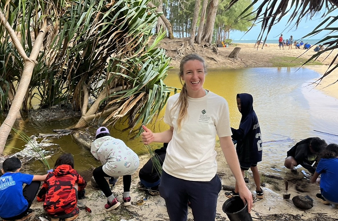 Julie Zill leads a group of people planting plants along a stream in Hawaii