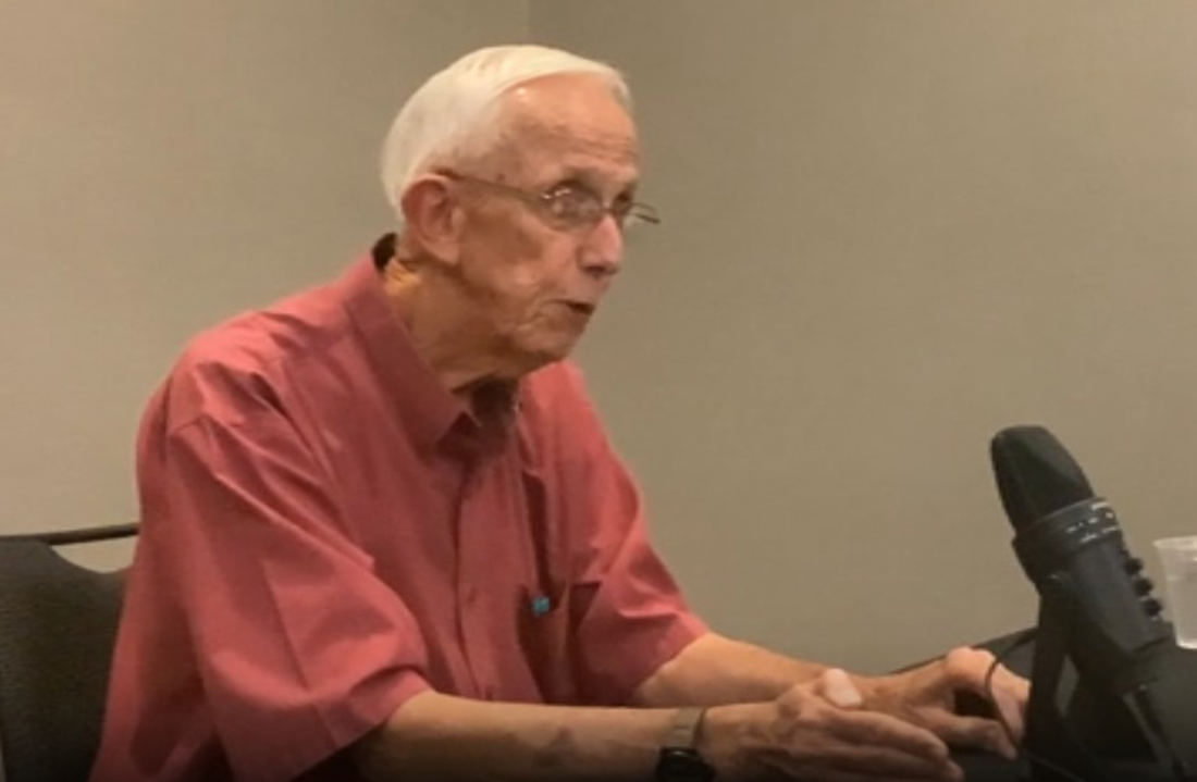 man in red shirt and white hair sits in front of a microphone.